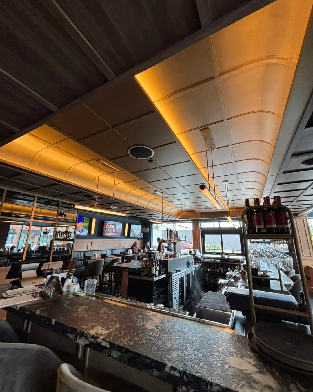 Bar area with an illuminated cove ceiling and linear pendant fixtures above the counter